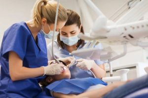 Dental professionals in blue scrubs and masks performing a clinical procedure on a patient in a modern dental setting